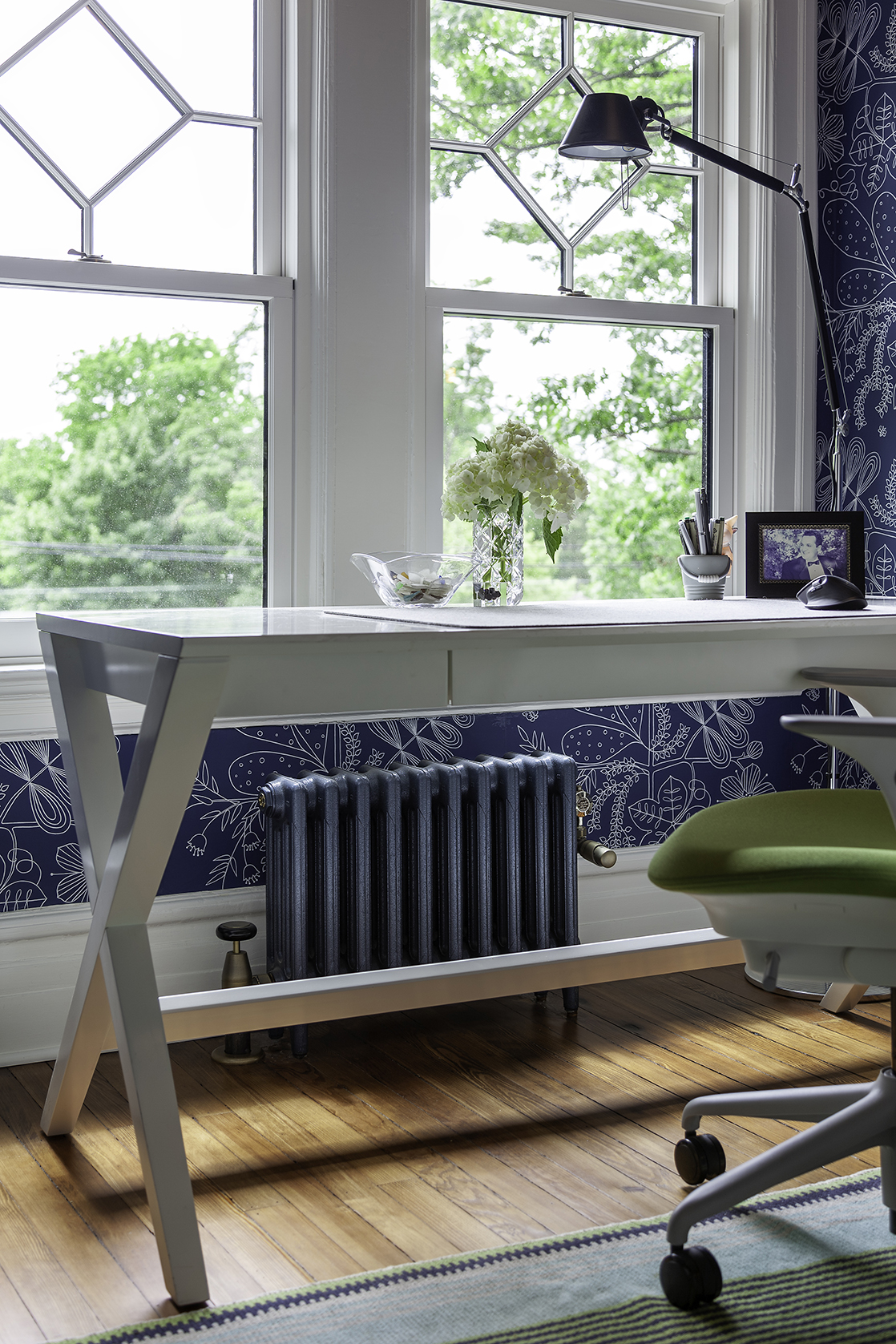 Blue steam cast iron radiator under window fitted with steam TRV (thermostatic radiator valve) in study with blue botanical wallpaper